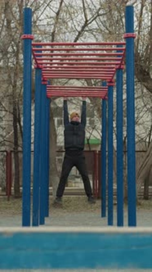 Coach Swinging on Iron Bar in Urban Outdoor Fitness Area with Football in Background
