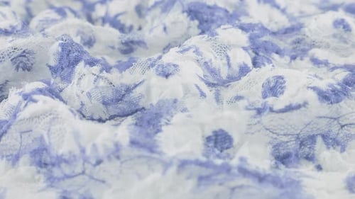 Close-up view of the light textured lace fabric in white and blue tones with a floral pattern rotate
