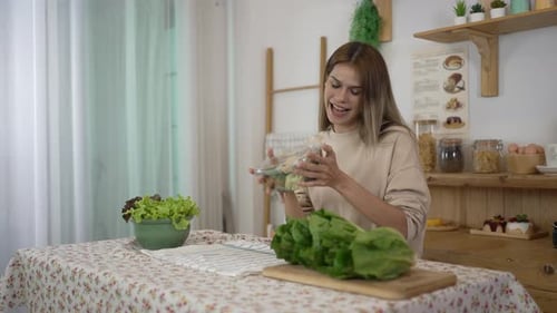 Young Woman Prepares Salad While Using Phone