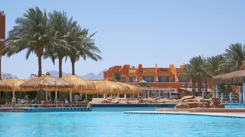 Empty Deck Chairs Under Straw Shade Umbrellas on Swimming Pool Side in Tropical Resort Summer