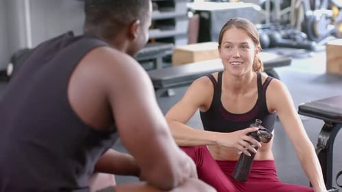 Fit young Caucasian woman chats with an African American man at the gym