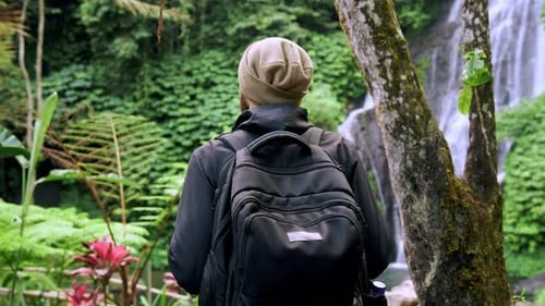 Traveling Man Walking in Green Nature of Forest Landscape to Mountain Waterfall