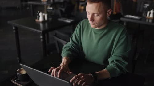 Hübscher Mann im grünen Pullover arbeitet mit Laptop im Café Junger erwachsener Mann mit tragbarem Computer