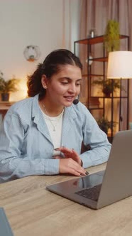 Young Female Customer Service Representative with Headset Using Laptop Computer at Home Office Table