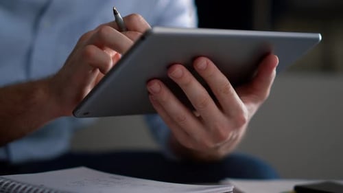Geschäftsmann erforscht Tablet-Computer, analysiert Finanzdaten und schreibt Notizen im Home Office