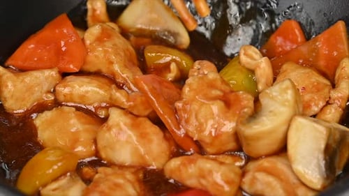 Woman eating chicken with vegetables and sweet sauce in a black pan at a chinese restaurant