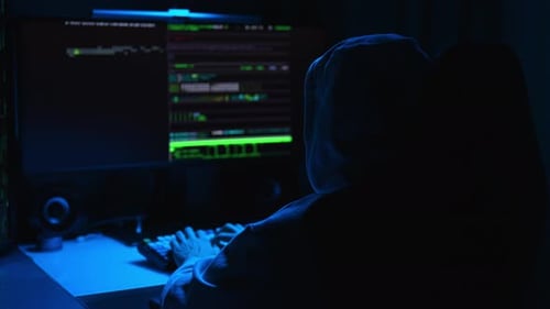 Vista traseira do hacker com capuz digitando no teclado quebrando a senha usando um PC de mesa sentado em
