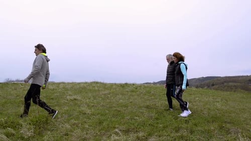 Group Of Senior Runners Walking Outside On The Green Hills.