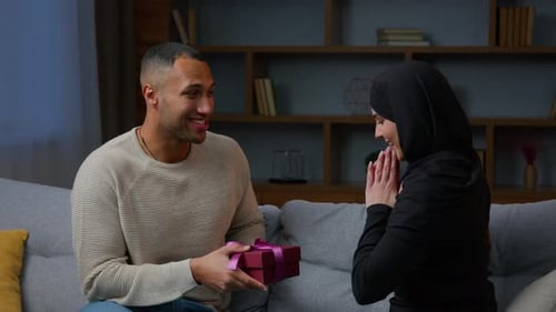 Loving Couple Exchanging Gifts at Home on Sofa