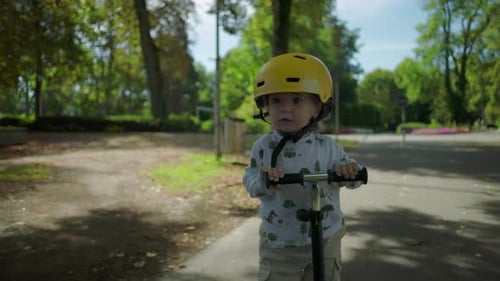 Toddler riding scooter smiling with joy, wearing yellow helmet, front view, enjoying playful