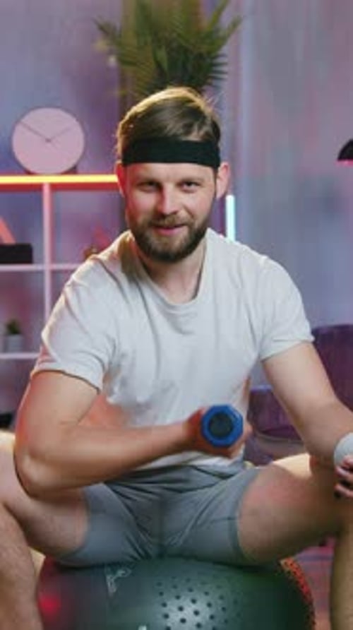 Handsome Positive Active 30Aged Bearded Man in Training Clothes and Headband Sitting on Rubber
