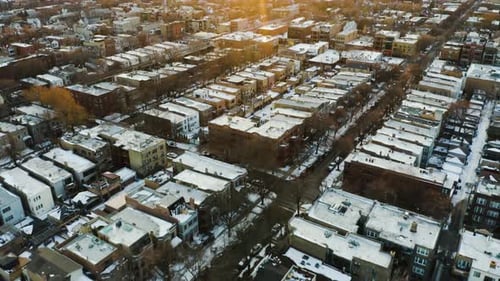 Aerial of dense urban city blocks with snow on rooftops, tilt up to reveal sunset