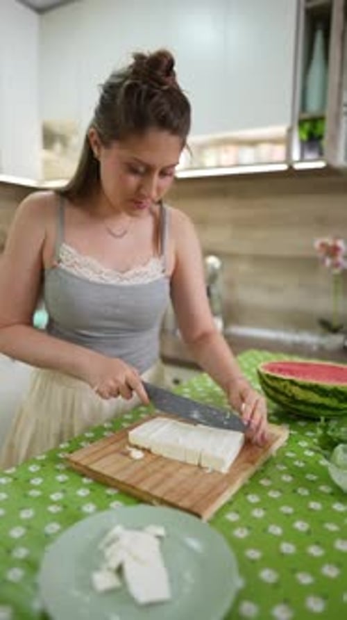 Jeune femme tranchant du fromage feta sur une planche à découper en bois dans une cuisine
