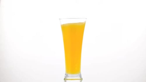Ice Cube Falling Into Glass of Orange Juice