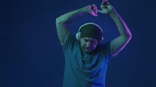 A Man Wearing White Wireless Headphones Listens to Music and Dances Vigorously A Man in a Studio on