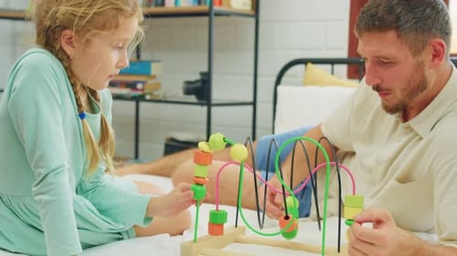 Father and Daughter Playing with Bead Maze on Bed