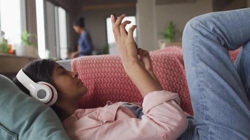 Video einer entspannten Frau aus Biracial mit Kopfhörern, die auf dem Sofa liegt und das Smartphone