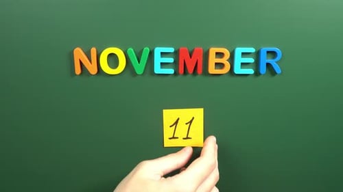 Hand sticking a sticker 11 November calendar day on school board. 11 date of November. Eleventh