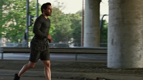 Athletic Young Man in Earphones and Sports Outfit is Jogging in the Street. He is Running in an Urb