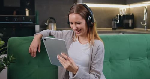 Hermosa joven caucásica en ropa casual con auriculares usa una tableta digital y sonríe