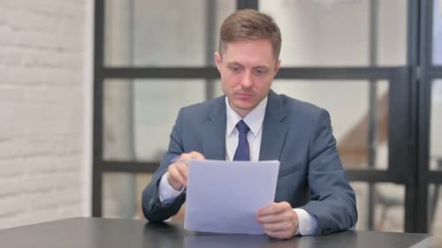 Man in Suit Reviews Documents at Desk