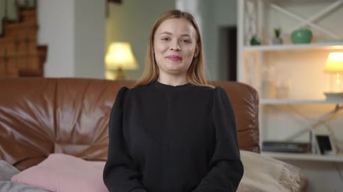 Happy woman holding money sitting on couch indoors