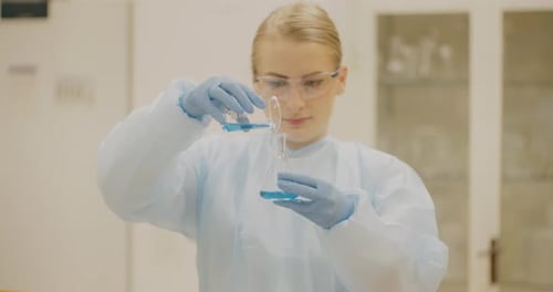 Young Woman Pouring Blue Liquid in Laboratory