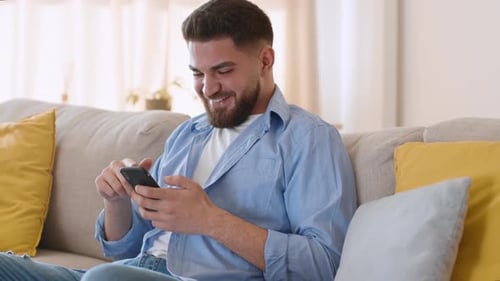 Smiling Man Using Smartphone on Sofa at Home