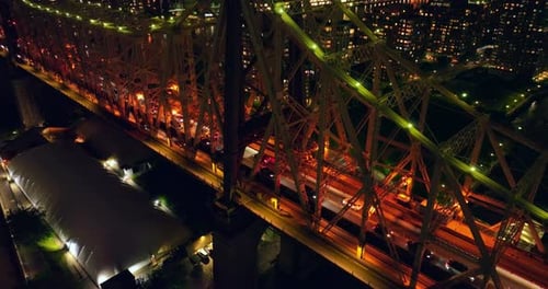 Orange and green backlight at Queensboro Bridge. Numerous cars going by the bridge at night