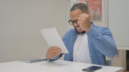 African Businessman Celebrating Success on Tablet in Office