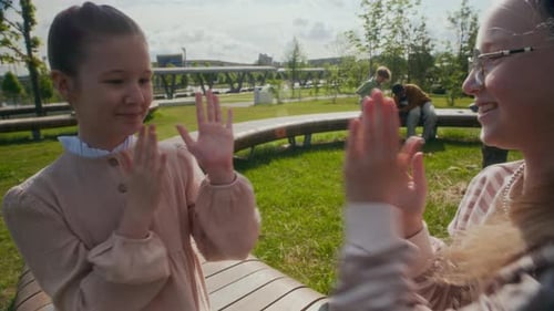 Duas alunas felizes sentadas no banco do parque e jogando aplausos