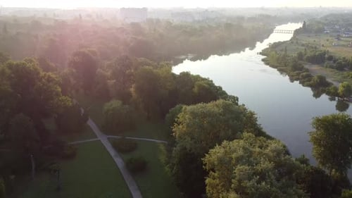 Green Trees in Park Calm River in City Multistorey Urban Buildings Sun Glare