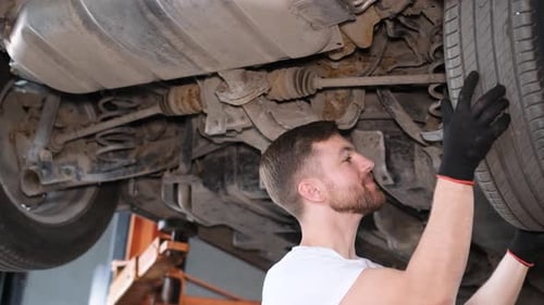 Handsome Professional Car Mechanic Inspects Car with Lift During Service