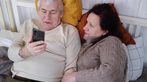 Mature Couple Relaxing in Bed With Smartphone