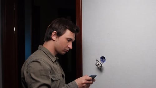 Eletricista instalando o interruptor de luz e instruções de consultoria no smartphone