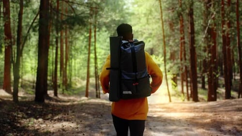 An African American Traveler with a Backpack Walks Through the Forest