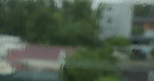 Gouttes de pluie : fenêtre De grosses gouttes de pluie tombent sur une vitre pendant une averse d'été. Des gouttelettes d'eau se forment
