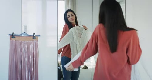 Foto autêntica de uma jovem morena experimentando, atrás do espelho, em um quarto, novos vestidos, ela