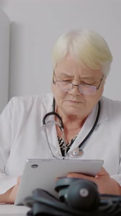 Pantalla vertical Doctora que usa una tableta para procesar los datos de los pacientes para su análisis médico.