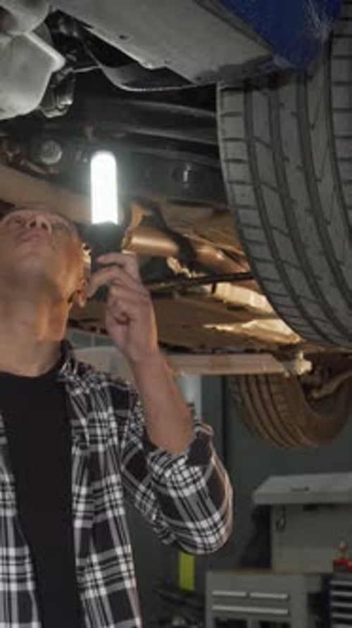 Focused Man Inspecting a Lifted Car with a Flashlight in a Sleek Workshop