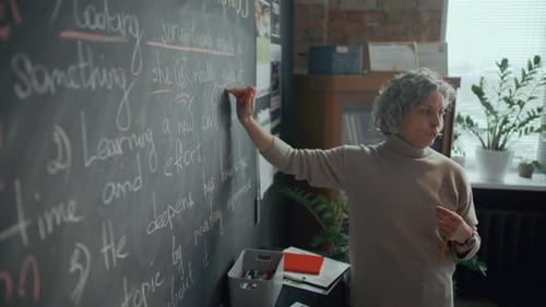 Teacher Explains Lesson at Chalkboard in Classroom