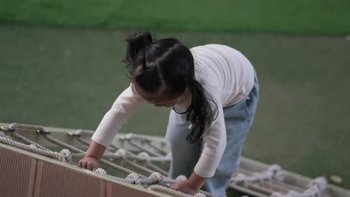 glückliches Mädchen spielt mit Kletterseilnetz auf einem Spielplatz im Freien im Park