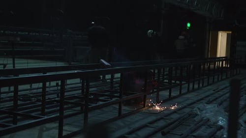Welder Works on Iron Railings Inside Dark Industrial Room