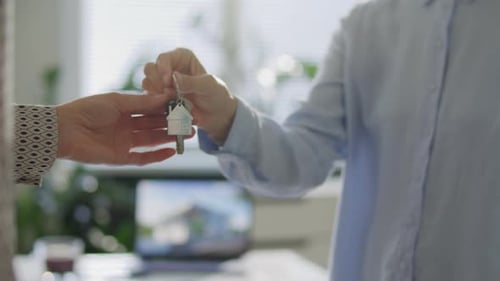 Close Up of Real Estate Agent and Client Exchanging House Keys in Office