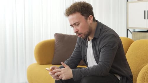 Worried Man Looking at Phone on Couch