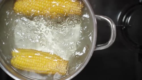A close-up shot and a top-down view of the silver pot with boiling corn on a black gas stove. Slow-m