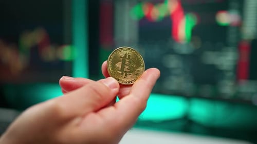 Hand Holding Bitcoin Coin in Front of Market Chart