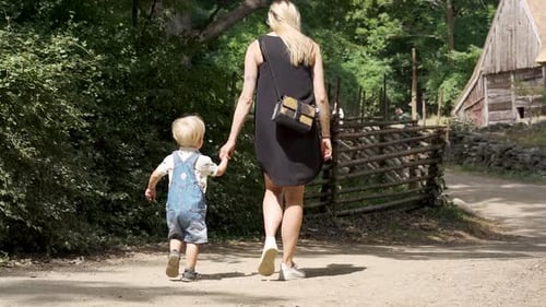 Young Caucasian mother and two years old boy holding hands walking down a trail in a rural village i