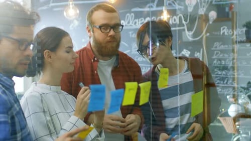 Team Brainstorming Ideas on Glass Wall in Office