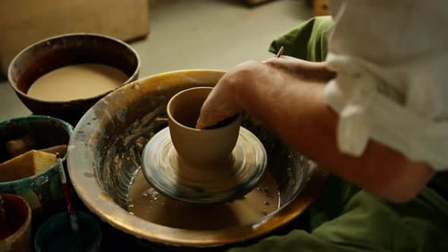 Close-up of potter's hands covered with clay making beautiful vase on throwing wheel in pottery